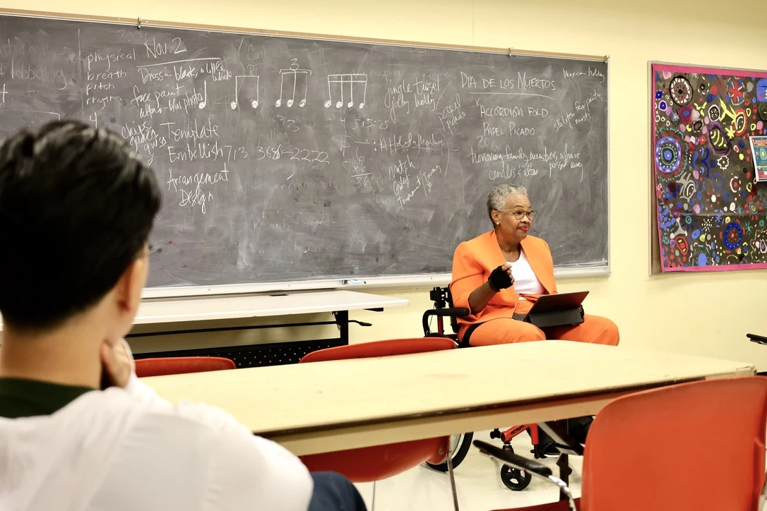 An educator using a wheelchair teaching a music class at the chalkboard