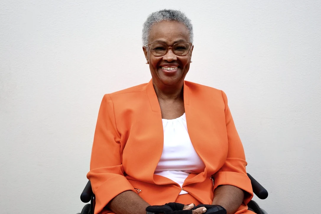 Woman in an orange blazer, using a wheelchair, bright studio portrait