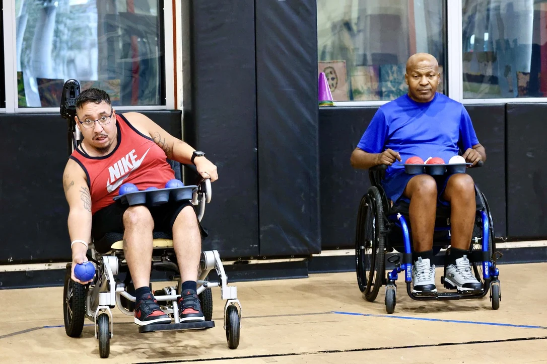 Two adaptive athletes in sports wheelchairs competing in a gymnasium