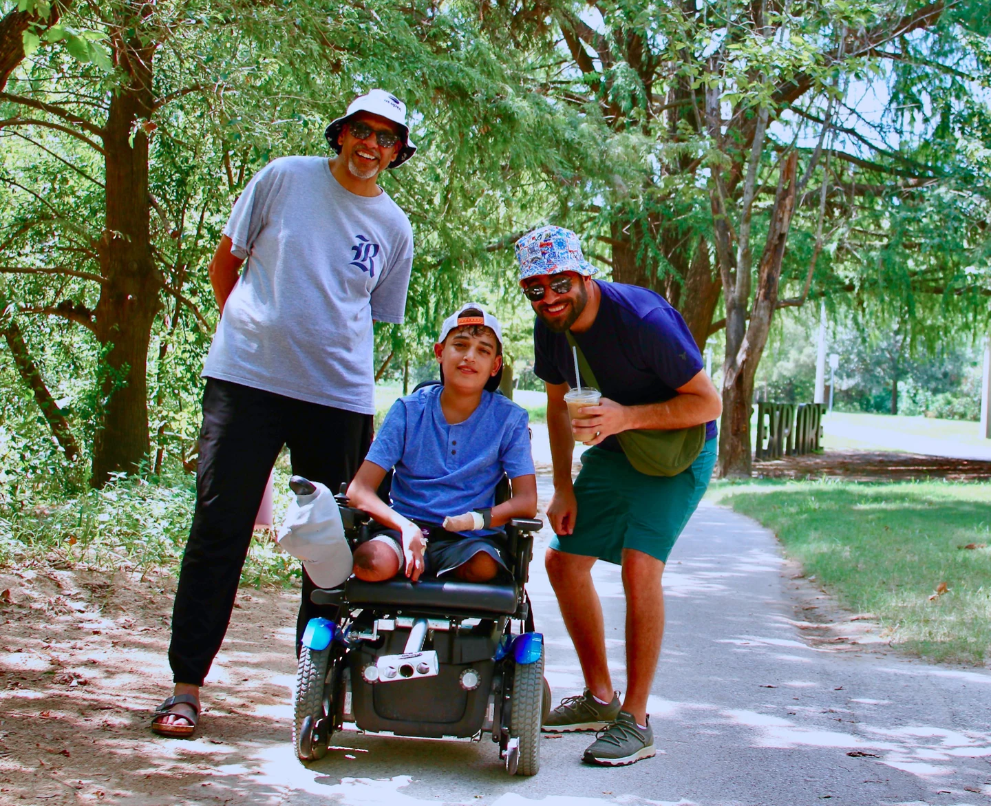 Three friends, one using a power wheelchair, laughing together on a wooded trail
