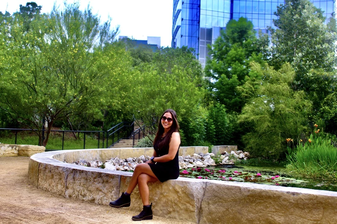 Woman seated in the same garden courtyard wearing sunglasses, environmental portrait